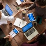 A diverse group of professionals brainstorming in a modern workspace with laptops and notebooks.